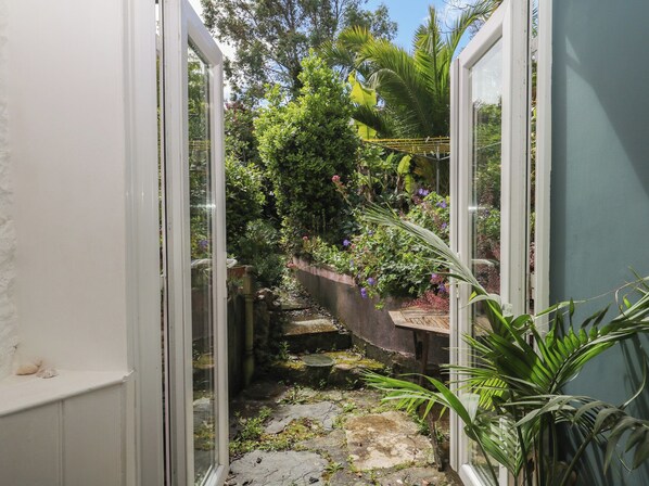 A narrow garden pathway leading to a door, surrounded by lush greenery and a small water feature. - Tiller Cottage (Dartmouth)