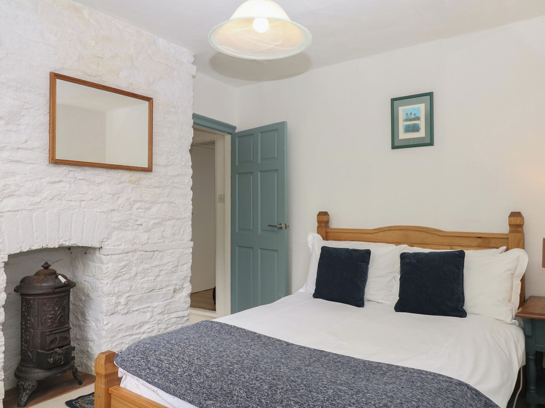 Une chambre à coucher avec un lit, une cheminée, une porte et un tableau encadré au mur.