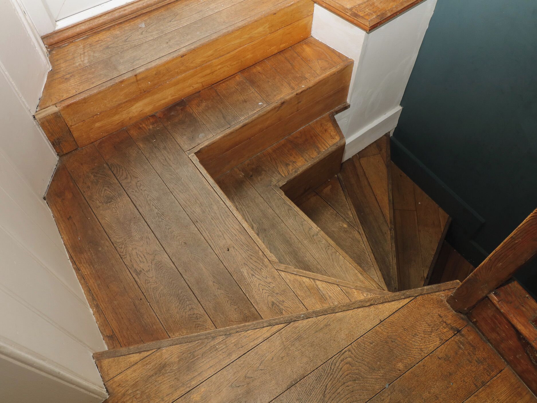 A wooden staircase with a white wall and a dark door at the bottom.