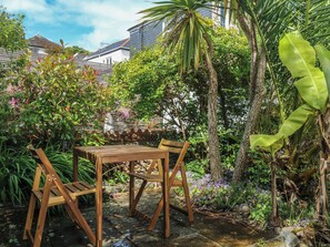 Ein Holztisch mit Stühlen in einem Garten, der verschiedene Pflanzen und eine Steinmauer zeigt.