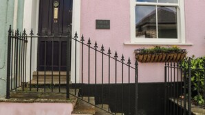 Un edificio rosa con una puerta negra, una ventana con marco blanco y un letrero que dice 'TILLER COTTAGE'.