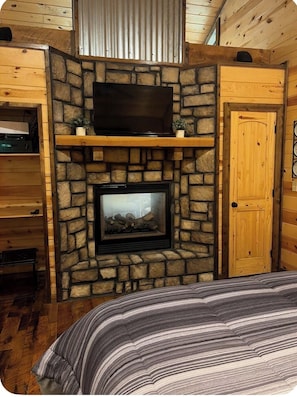Ein gemütliches Zimmer mit Kamin aus Stein, einem darüber montierten Fernseher und Holzwänden.