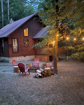 Ein rustikales Blockhaus mit einer Terrasse, umgeben von Bäumen und Kies.