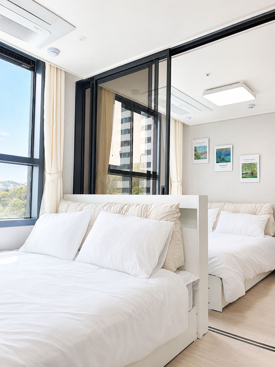 A modern hotel room with a large bed, a window with curtains, a mirror, and artwork on the wall.