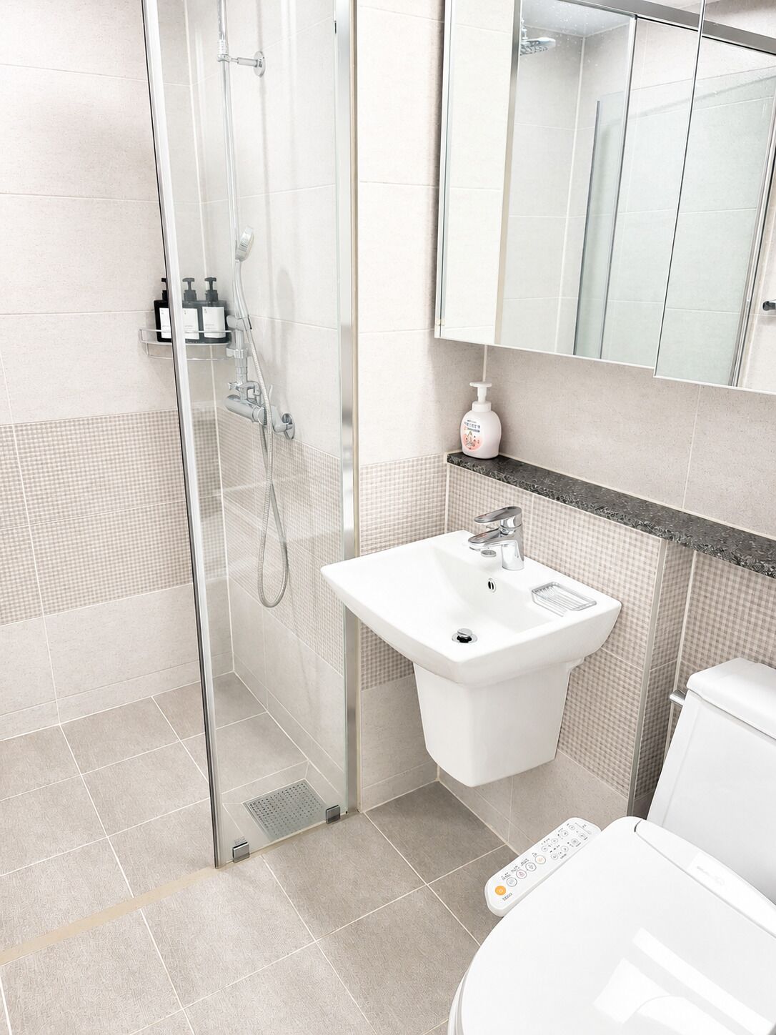 Un baño moderno con cabina de ducha de vidrio, un lavamanos blanco y un inodoro.