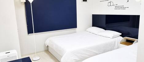 A bedroom with two beds, a desk, a lamp, and a wall with cat illustrations.
