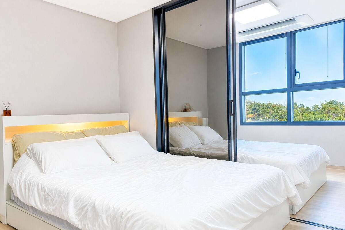 Ein Schlafzimmer mit zwei Betten, einem großen Fenster und Blick auf Grünfläche.