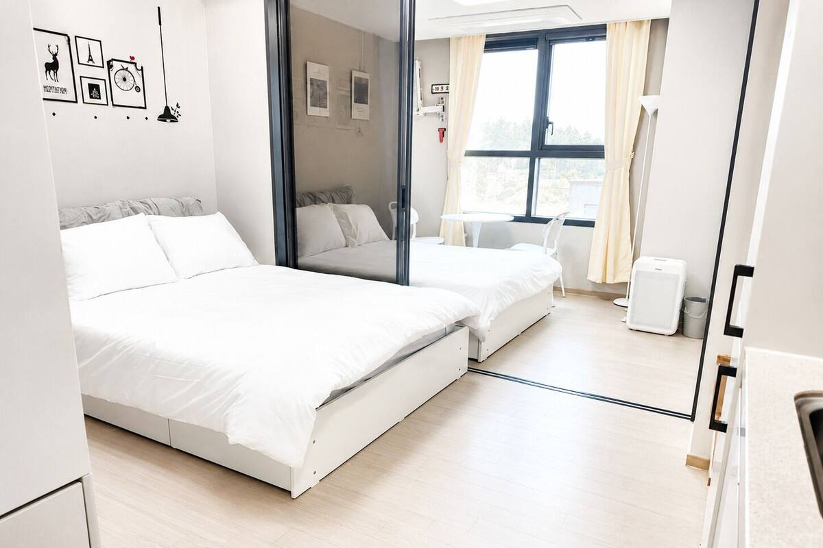Ein modernes Hotelzimmer mit zwei Betten, einem kleinen Tisch, einem Stuhl, einem Fenster mit Vorhängen und einer Wand mit gerahmten Bildern.