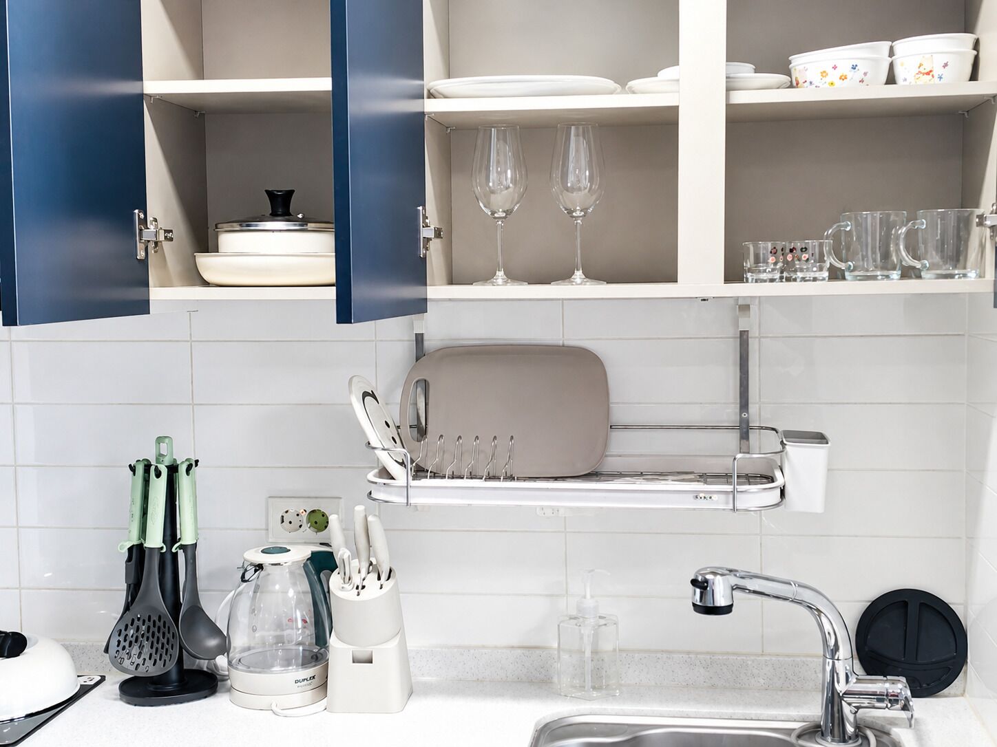 Una cocina con armarios blancos, un lavabo y diferentes utensilios.