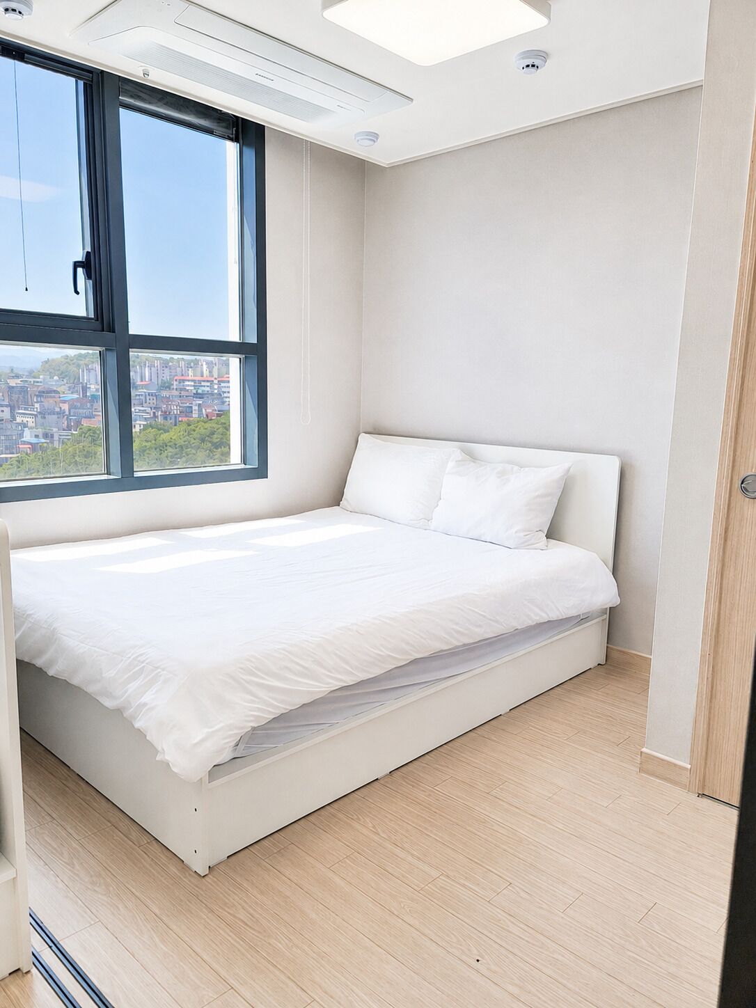 Un dormitorio con cama, ventana y vistas a la ciudad.
