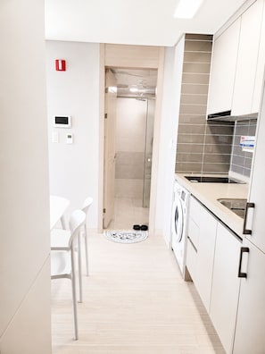Una cocina moderna con lavadora, una zona de comedor con sillas y un espacio para la ducha.