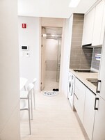 Una cocina moderna con lavadora, una zona de comedor con sillas y un espacio para la ducha.