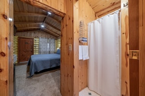 Ein Interieur einer Holzhütte mit einem Bett, einer Duschvorhang und einer Tür zu einem anderen Raum.