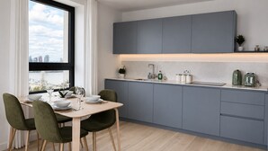 A modern kitchen with grey cabinets, a dining table with chairs, and a view of the city through a window. - Stylish Greenwich flat near The O2 with Balcony & Wi-Fi (London)