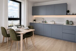 Eine moderne Küche mit grauen Schränken, einem Esstisch mit Stühlen und Blick auf die Stadt durch ein Fenster.