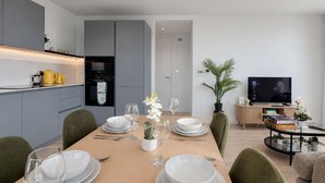 A modern dining area with a wooden table set for four, surrounded by green chairs. - Stylish Greenwich flat near The O2 with Balcony & Wi-Fi (London)