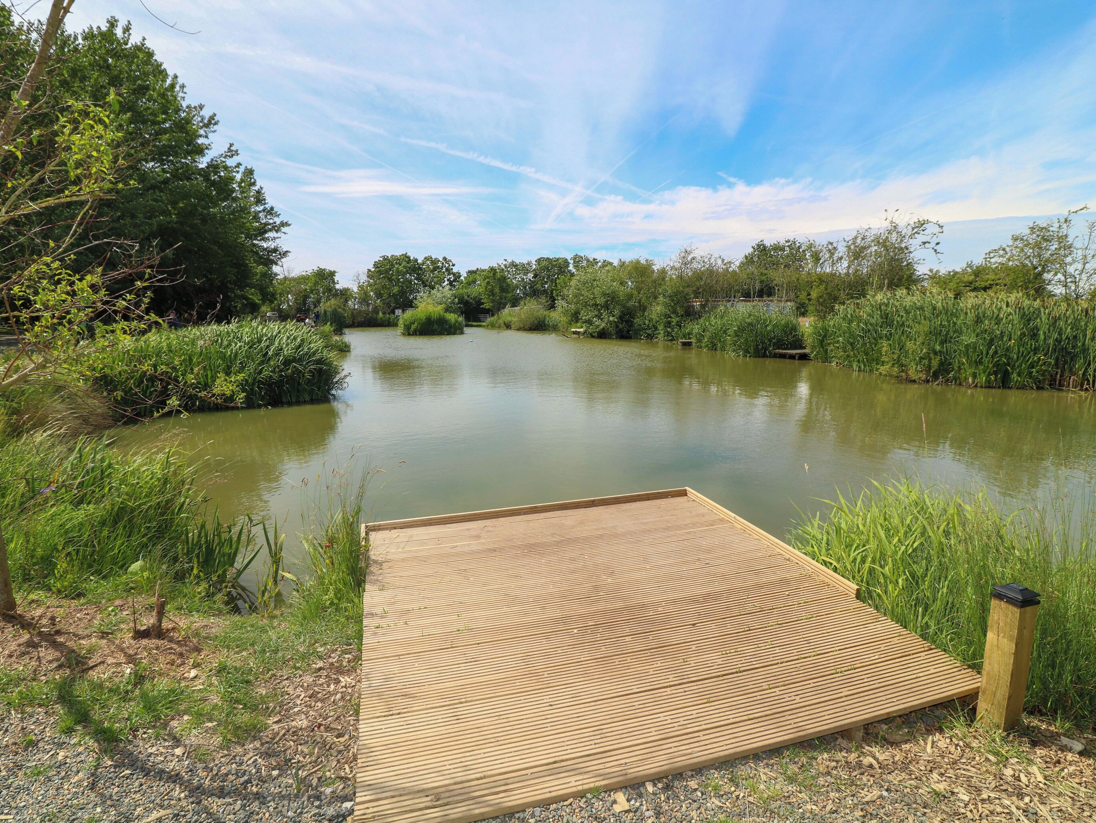 Een houten terras aan een rustige rivier, met weelderige begroeiing en bomen op de achtergrond.