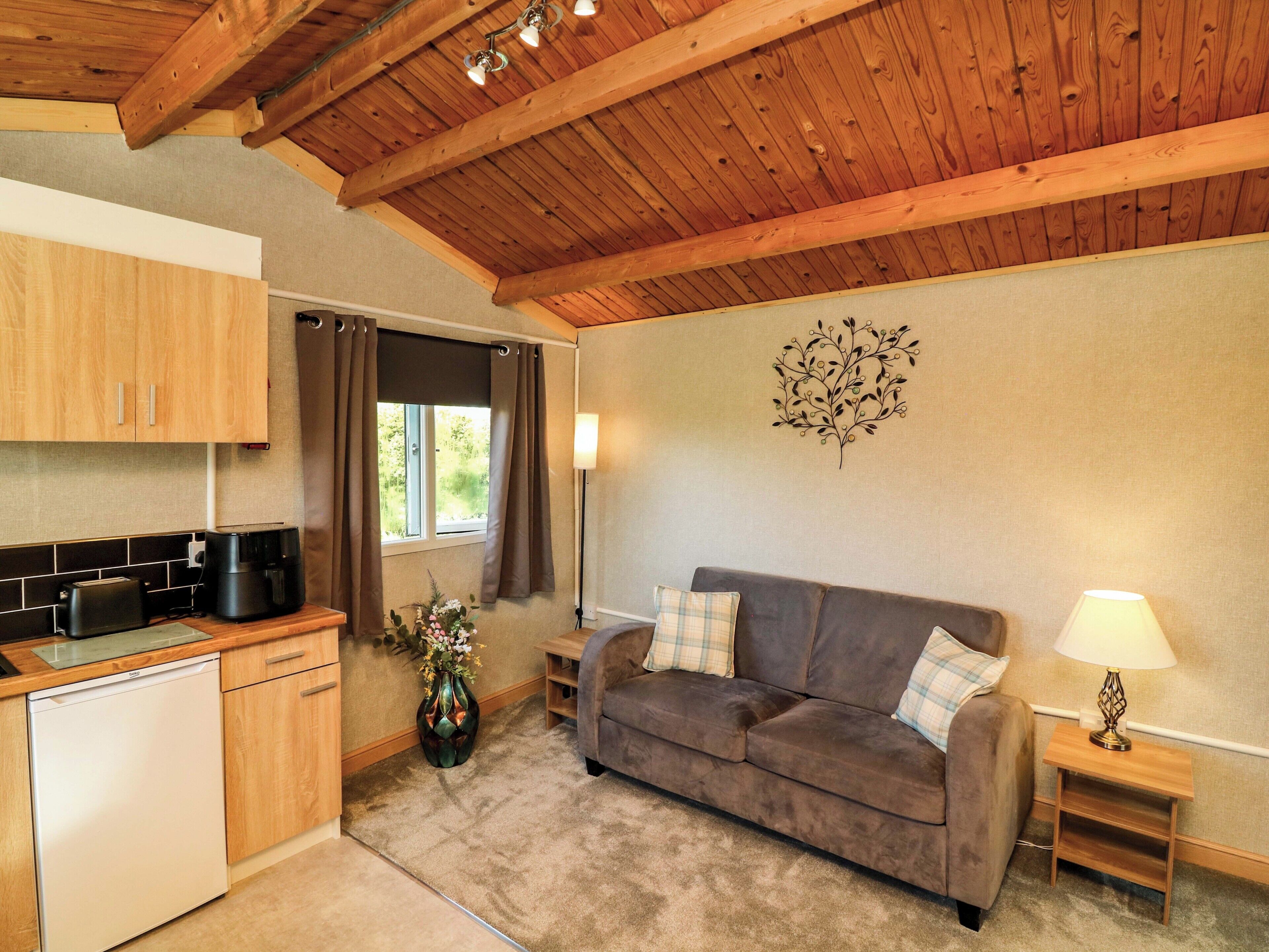 A compact kitchen with a dishwasher, a dining area with a brown sofa and a small table, and a decorative wall piece.