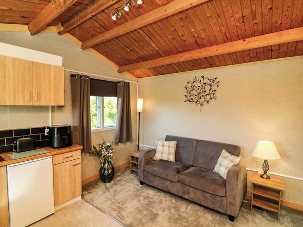 A compact kitchen with a dishwasher, a dining area with a brown sofa and a small table, and a decorative wall piece.