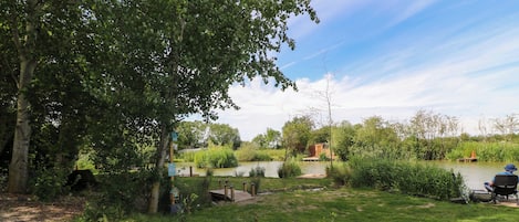 A riverside campsite with a wooden deck, a small shed, and a fishing area.
