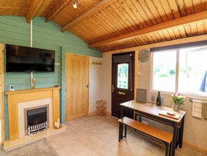A room with a wooden ceiling, a fireplace, a television, a clock, and a window with a view.
