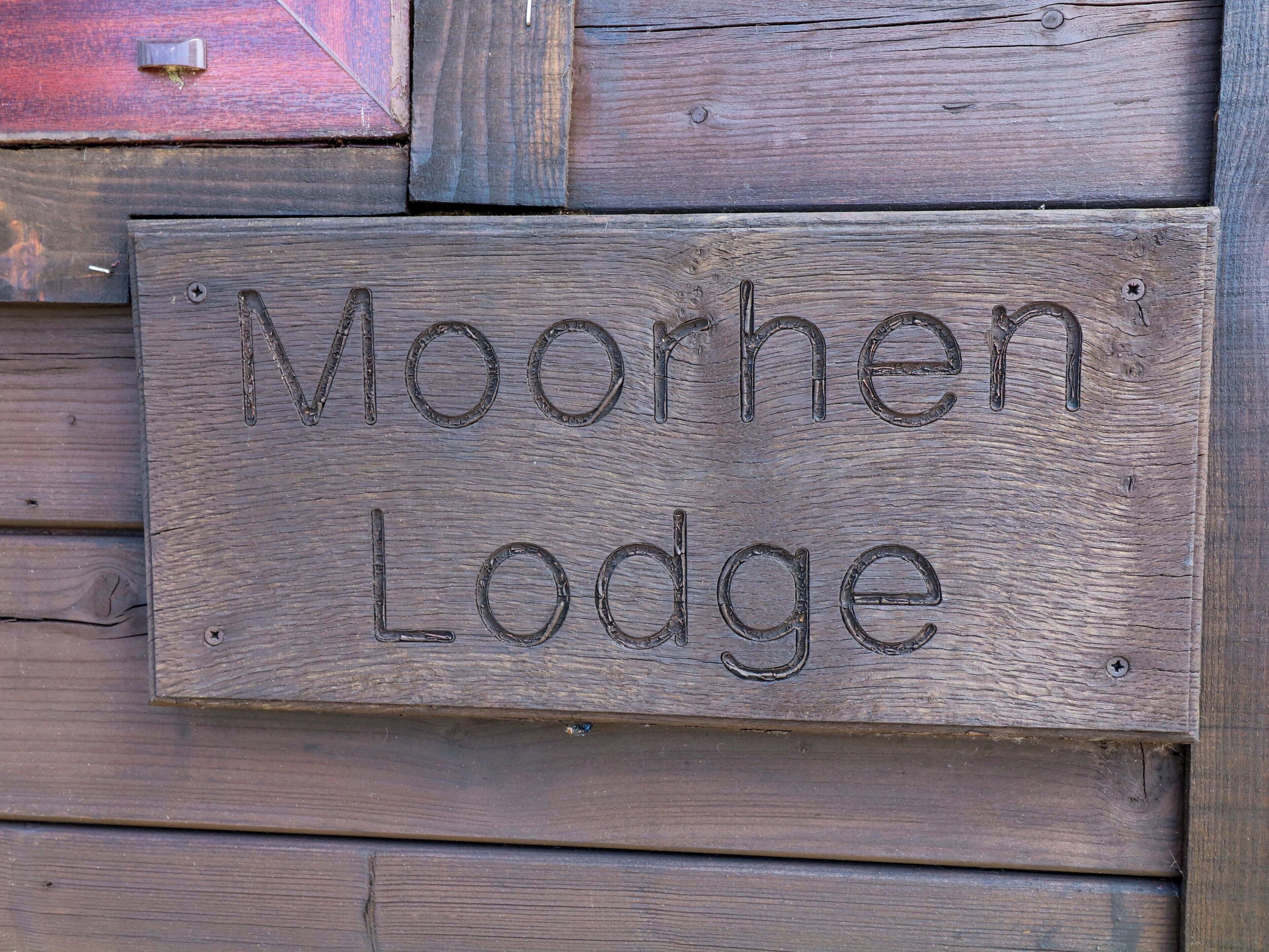 En träskylt med texten ”Moorhen Lodge” som är fastsatt på en trävägg.