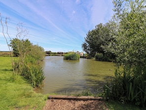 A tranquil riverside setting with a wooden bridge, lush greenery, and a clear sky.