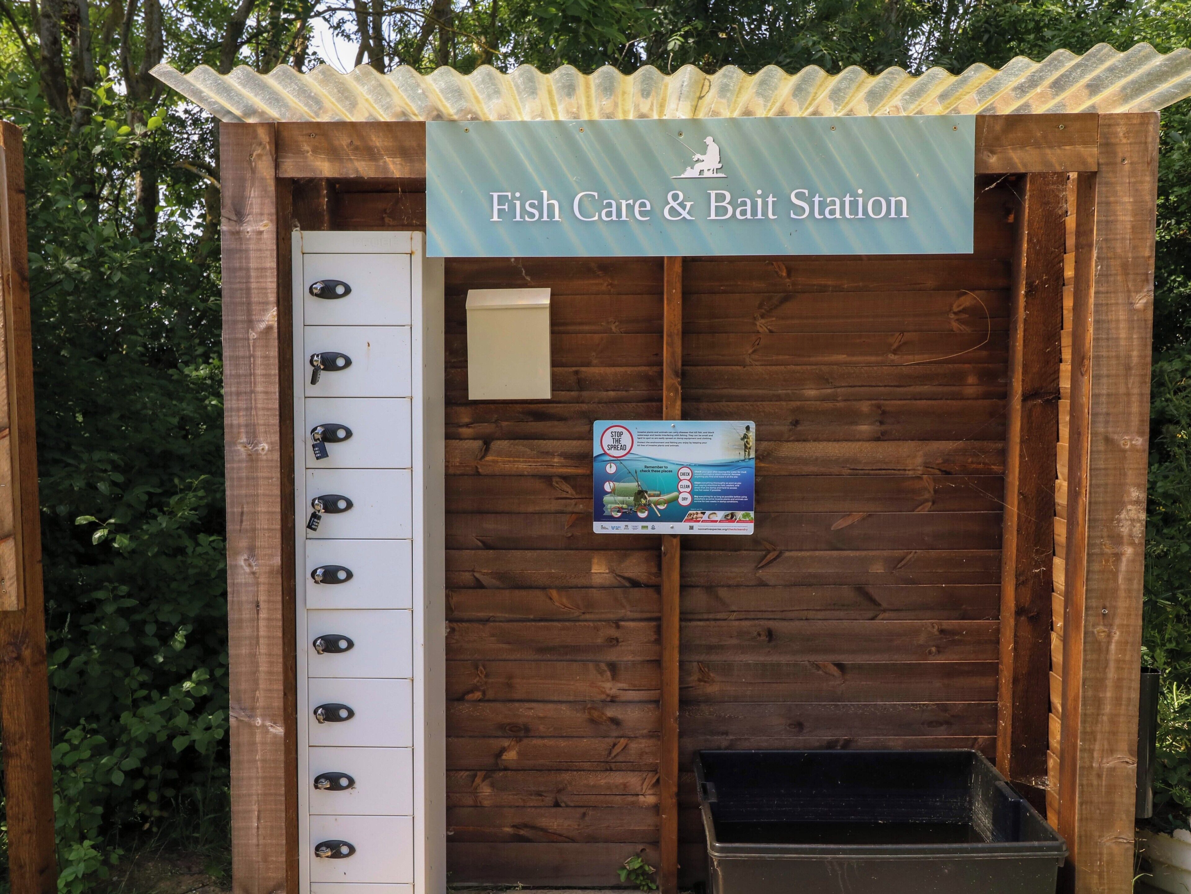 A wooden structure labeled 'Fish Care & Bait Station' with a signboard and a trash bin.