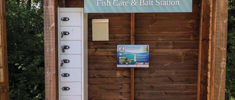 Estructura de madera con un letrero que dice 'Fish Care & Bait Station' y un bote de basura.
