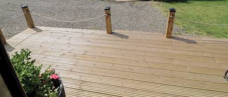 A wooden deck with a rope barrier, a gravel path, and a body of water with vegetation.