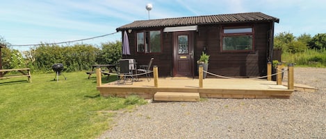 A wooden cabin with a gravel driveway, a picnic table, and a barbecue grill.