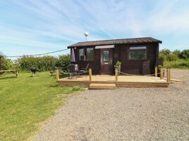 A wooden cabin with a gravel driveway, a picnic table, and a barbecue grill.