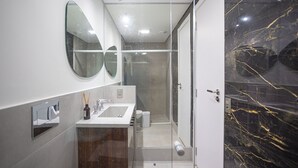 Une salle de bain moderne avec une douche à parois de verre, un meuble-lavabo avec miroir et un mur d’accent en marbre.