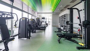 Une salle de sport équipée de divers appareils d’exercice, dotée de grandes fenêtres et d’un sol recouvert d’une moquette verte.