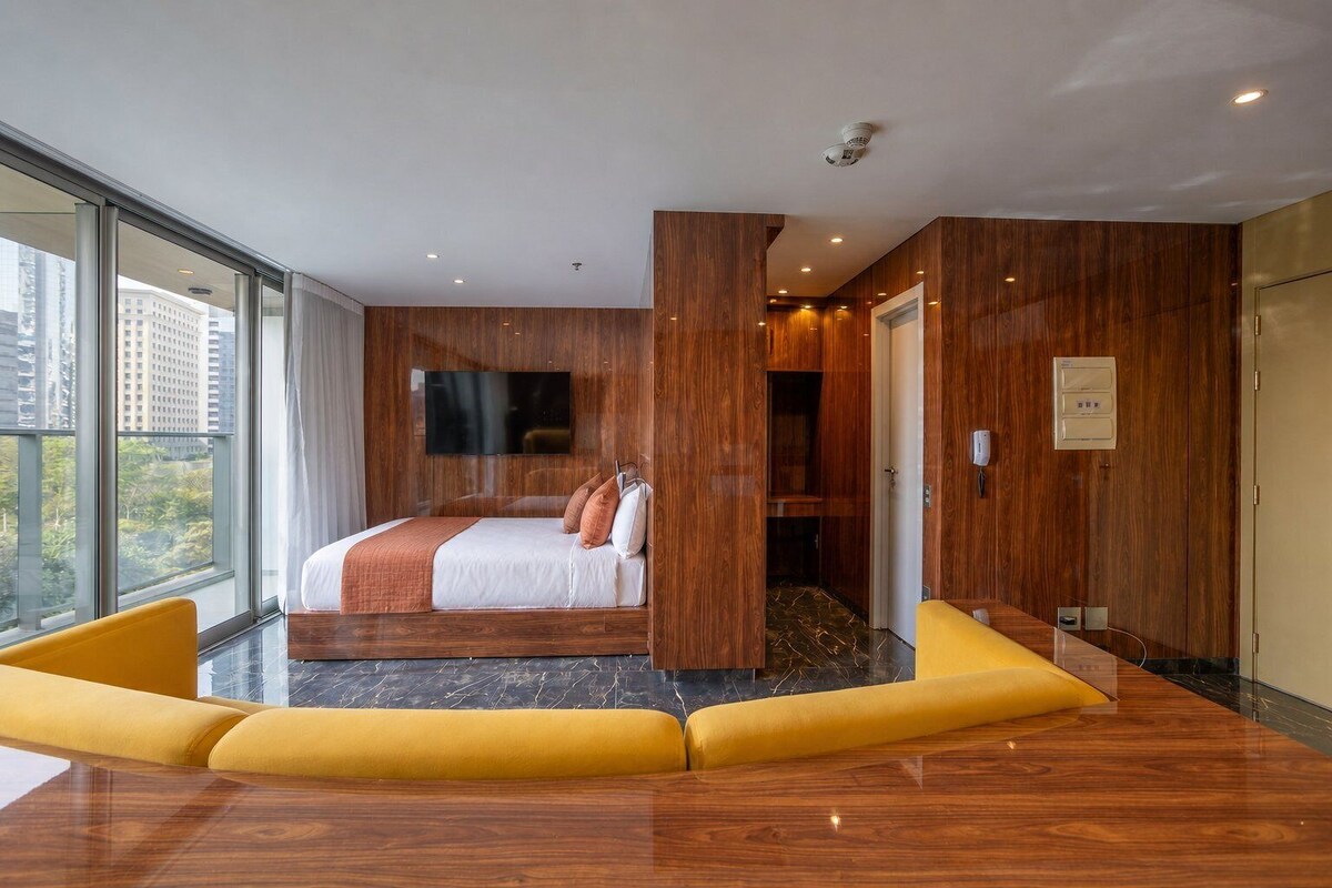 A modern hotel room with a large bed, a flat-screen TV, and a view of the city.