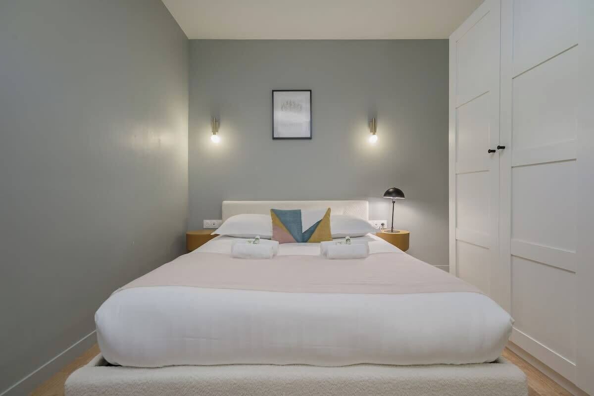 Ein ordentlich bezogenes Bett mit weißen Leinen, ein Kissen mit geometrischem Muster und zwei Nachttischlampen.