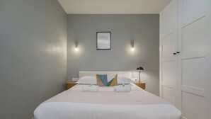 A neatly made bed with white linens, a pillow with a geometric design, and two bedside lamps. - Spacious apartment 8PAX in the center (Paris)