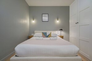 Ein ordentlich bezogenes Bett mit weißen Leinen, ein Kissen mit geometrischem Muster und zwei Nachttischlampen.