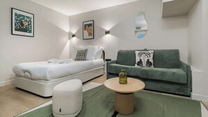 Ein modernes Schlafzimmer mit einem Bett, einer grünen Couch, einem runden Couchtisch und zwei Wandleuchten.