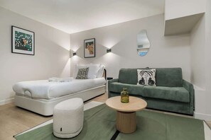 Ein modernes Schlafzimmer mit einem Bett, einer grünen Couch, einem runden Couchtisch und zwei Wandleuchten.