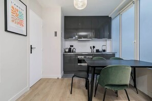Moderni keittiö, jossa on tummat kaapit, ruokapöytä tuoleineen ja riippuvalaisin.