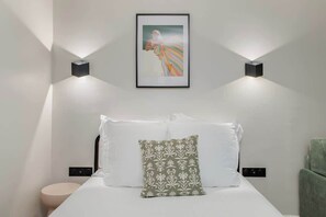 A neatly arranged hotel room with a bed, pillows, a framed artwork, and wall-mounted lighting. - Studio next to Montmartre and Pigalle (Paris)