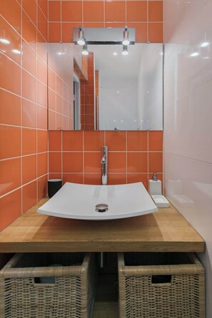 A bathroom with a white sink, orange tiles, a mirror, and wicker baskets. - Studio next to Montmartre and Pigalle (Paris)