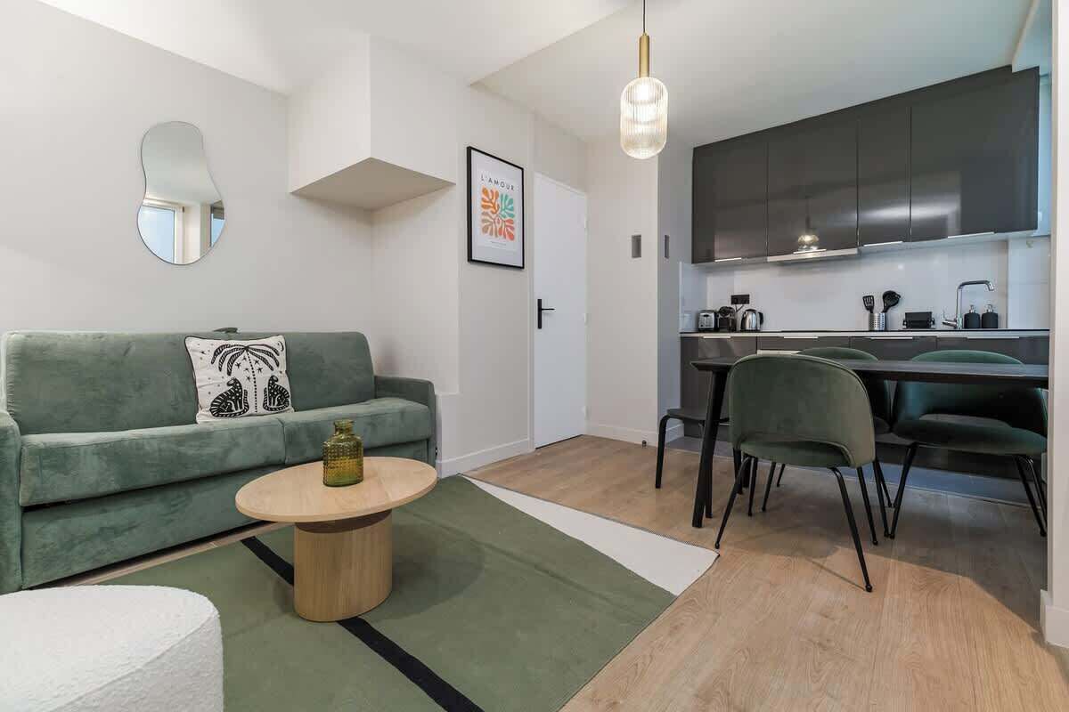 Una sala de estar moderna con un sofá verde, una mesa de centro redonda y una cocina con armarios oscuros y una mesa de comedor.