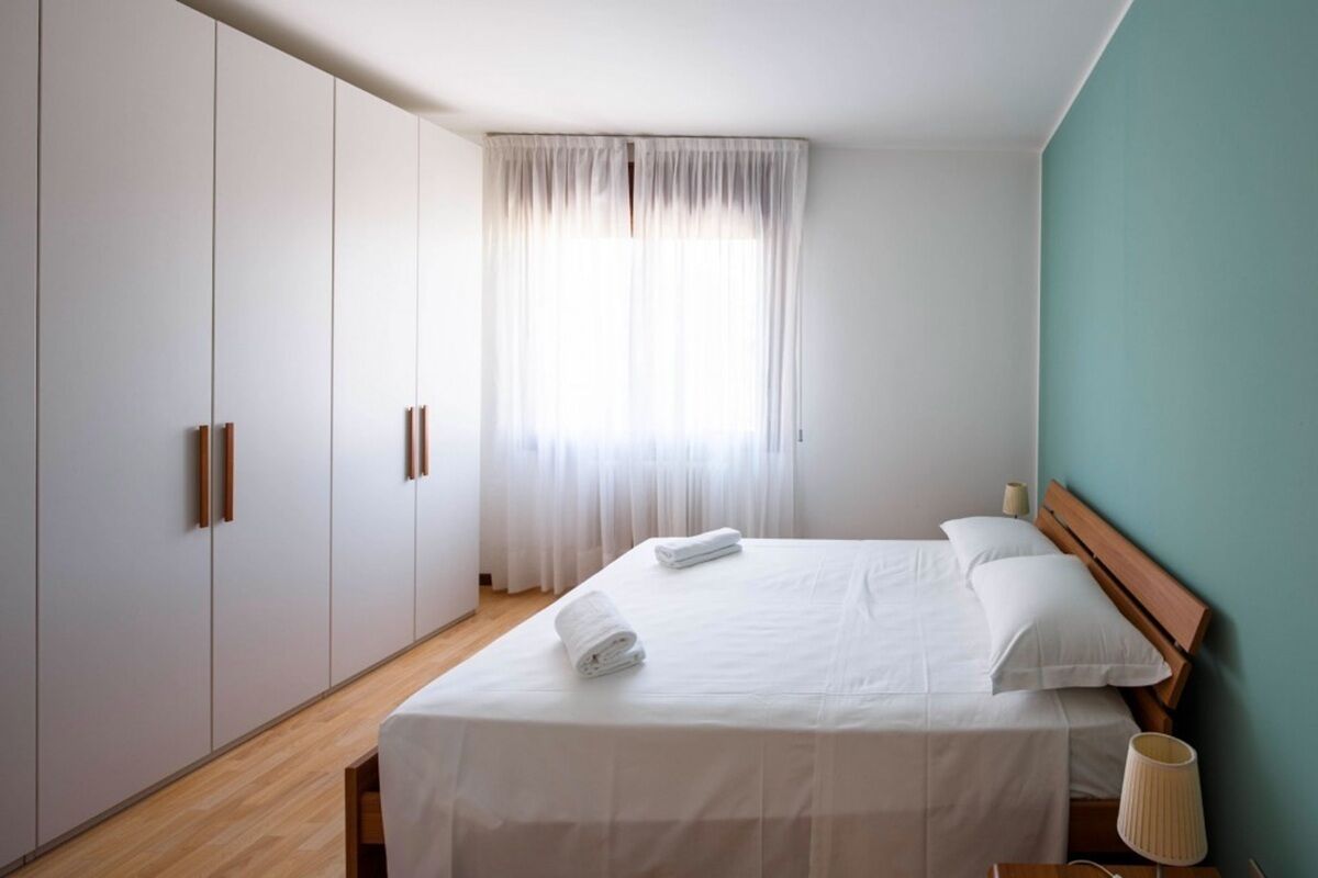 Een slaapkamer met een bed, een kledingkast, een raam met gordijnen en een lamp.