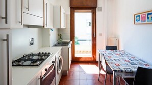 A compact kitchen with a stove, washing machine, and a dining area with a table and chairs. - Bright Family Retreat with Terrace, Garden & Beach Nearby (Lido)