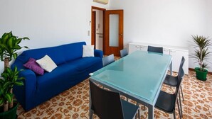 A room with a blue sofa, a glass-top table, and chairs. There is a door with a mirror, a radiator, and a potted plant. - Bright Family Retreat with Terrace, Garden & Beach Nearby (Lido)