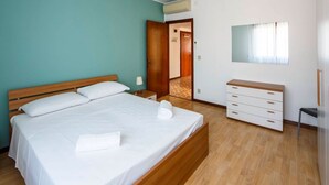 A bedroom with a bed, a dresser, a nightstand, and a door leading to another room. - Bright Family Retreat with Terrace, Garden & Beach Nearby (Lido)