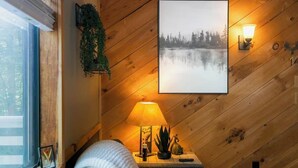 Een gezellige kamer met een houten wand, een lijst met afbeelding, een bedlamp en een raam.