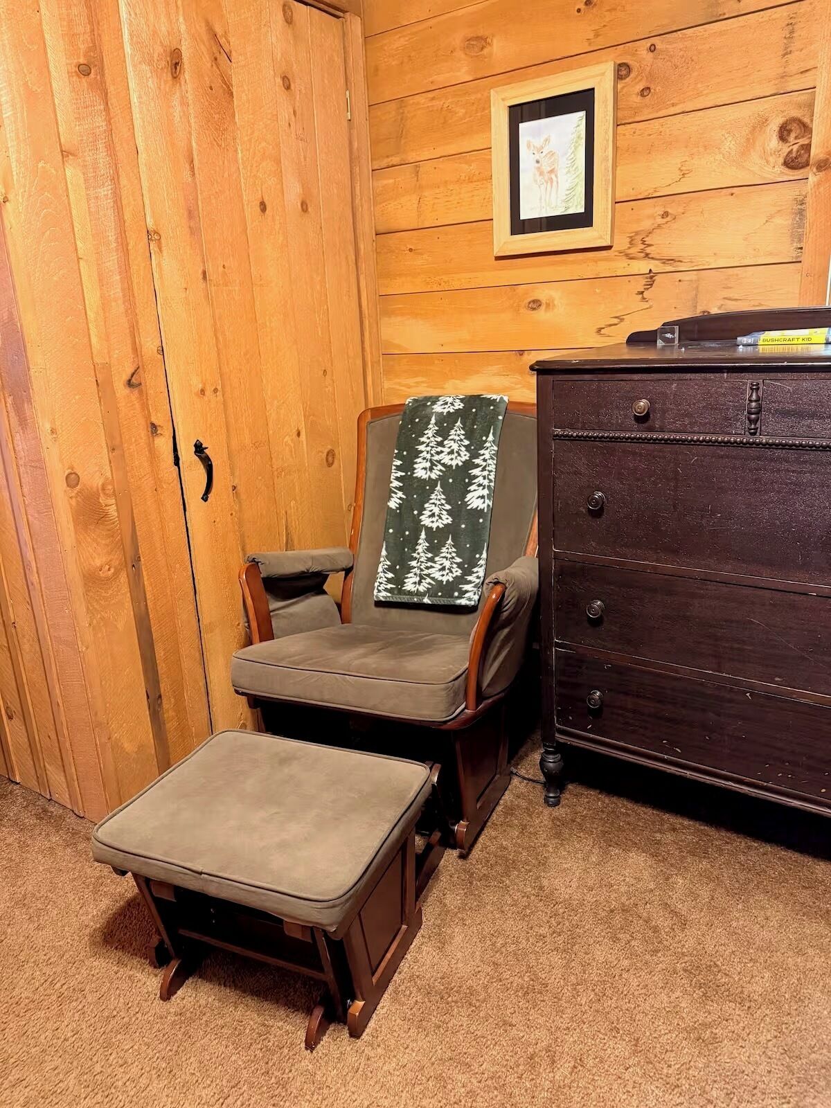 A wooden room with a chair, a small table, a dresser, and a framed picture on the wall.
